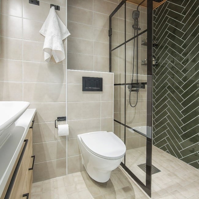 Kaunis kylpyhuone jossa seinä-WC, tyylikäs mustakehyksinen suihkuseinä sekä upeat laatat kalanruoto-laattaladonnalla.